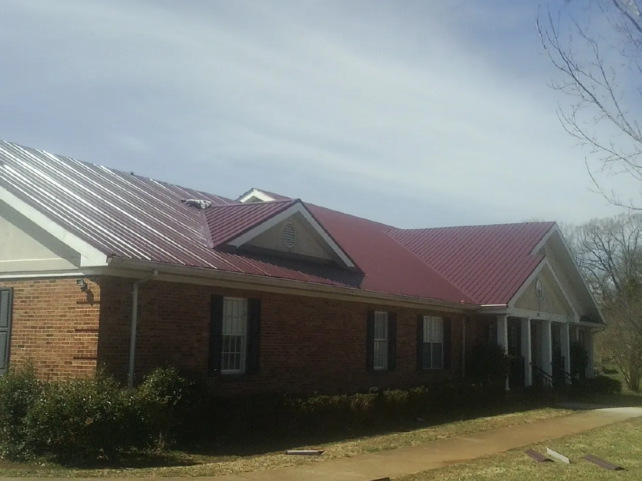 Red metal roof with gabled entries on a long brick building, from a Hail Damage Roof Repair job in Valyermo
