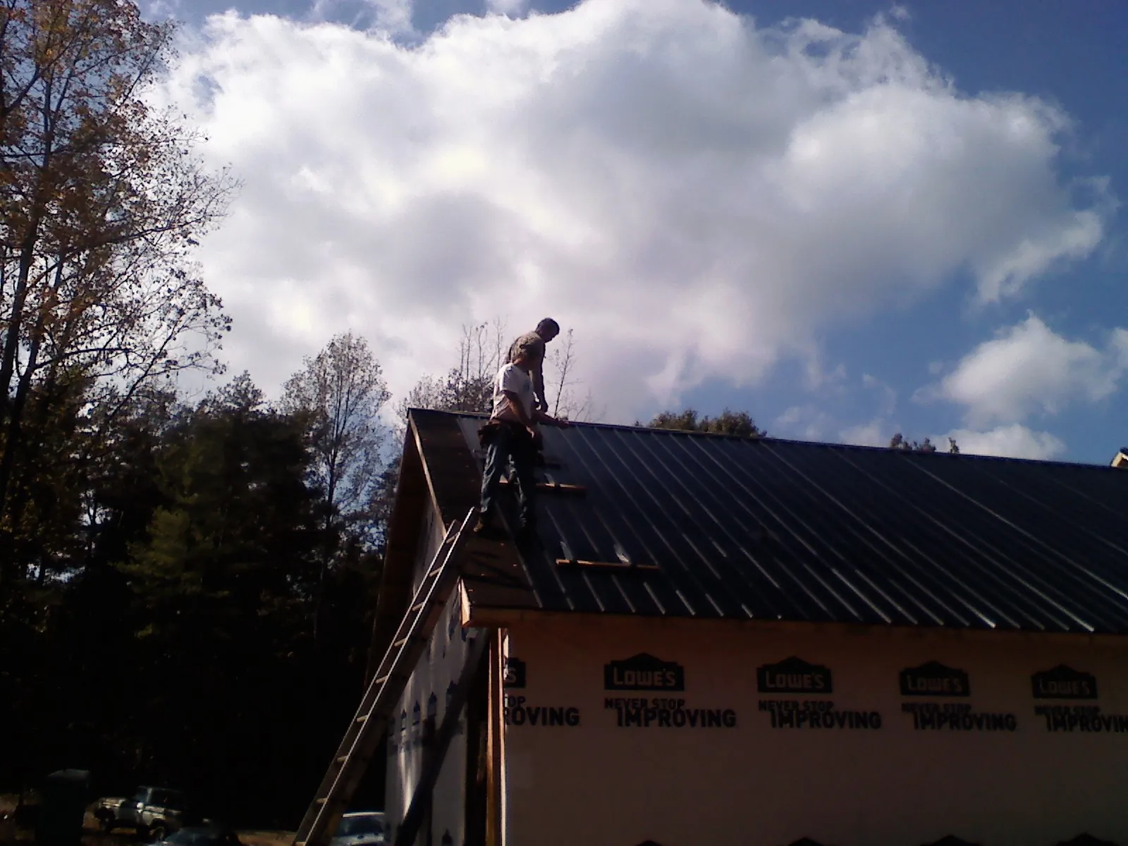 Roofer fastening dark metal panels high against a cloudy sky, from a Roof Inspection job in Valyermo